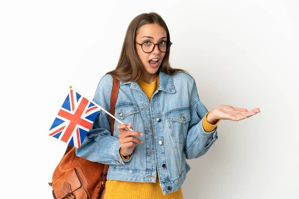 Young hispanic woman holding an United Kingdom flag over isolated white background with surprise expression while looking side
