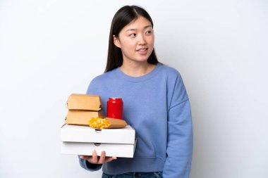 Beyaz arka planda hazır yemek tutan genç Çinli kadın yan tarafa bakıyor ve gülümsüyor.