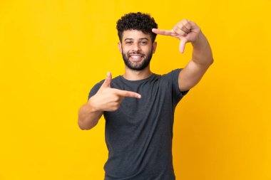 Faslı genç bir adam sarı arka planda izole edilmiş, odaklanmış bir yüz. Çerçeve sembolü