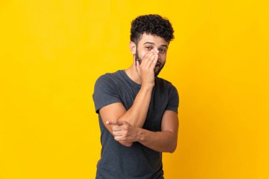 Sarı arka planda izole edilmiş genç Faslı bir adam bir ürün sunmak ve bir şeyler fısıldamak için kenarı işaret ediyor.