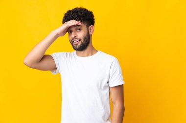 Sarı arka planda izole edilmiş genç Faslı bir adam yan tarafa bakarken sürpriz jest yapıyor.