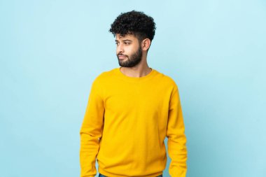 Faslı genç bir adam mavi arka planda izole edilmiş. Şüpheli hareketler yapıyor.