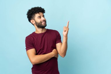 Faslı genç bir adam mavi arka planda izole edilmiş. Harika bir fikre işaret ediyor.