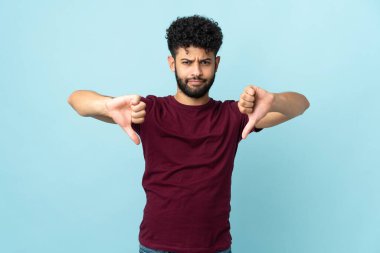 Mavi arka planda izole edilmiş genç Faslı iki eliyle baş parmağını gösteriyor.