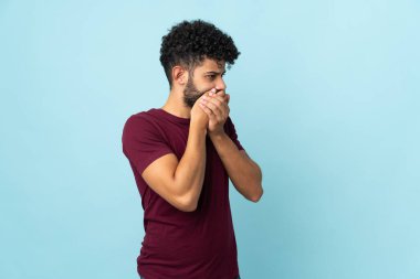 Genç Faslı adam mavi arka planda izole edilmiş, ağzı kapalı ve yana bakıyor.