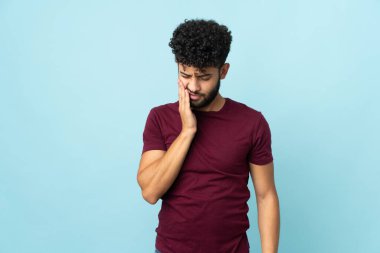 Faslı genç bir adam mavi arka planda diş ağrısı ile izole edilmiş.
