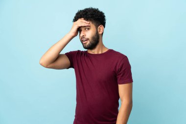 Faslı genç bir adam mavi arka planda izole edilmiş. Yan tarafa bakarken sürpriz jest yapıyor.