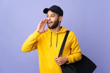 Spor çantalı genç Faslı adam mor arka planda izole edilmiş ağzı sonuna kadar açık bağırıyor.