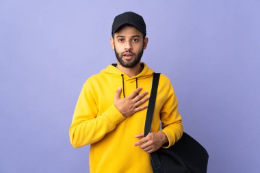 Spor çantalı genç Faslı adam mor arka planda izole edilmiş sağa bakarken şaşırmış ve şok olmuştu.