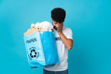 Genç Faslı bir adam, izole edilmiş arkaplanı yorgun ve hasta bir ifadeyle geri dönüştürmek için elinde kağıt dolu bir geri dönüşüm çantası tutuyor.