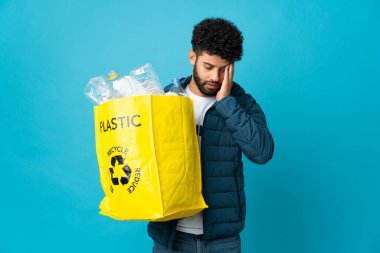 Genç Faslı bir adam elinde plastik şişelerle dolu bir çanta ile izole edilmiş arka planı baş ağrısıyla geri dönüştürüyor.