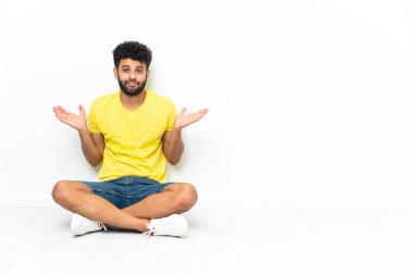 Genç Faslı yakışıklı bir adam izole edilmiş arka planda oturuyor. Kuşkuları var ve ellerini kaldırıyor.