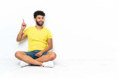 Genç Faslı yakışıklı adam izole bir zeminde oturmuş parmağını kaldırarak çözümü bulmaya çalışıyor.