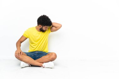 Genç Faslı yakışıklı adam, izole edilmiş arka planda, yerde oturuyor.