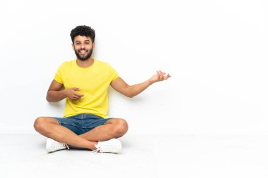 Genç Faslı yakışıklı bir adam izole edilmiş arka planda oturmuş gitar jesti yapıyor.