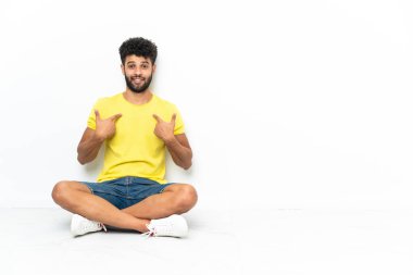 Genç Faslı yakışıklı bir adam yerde izole edilmiş bir şekilde oturuyor ve yüzünde sürpriz bir ifade var.