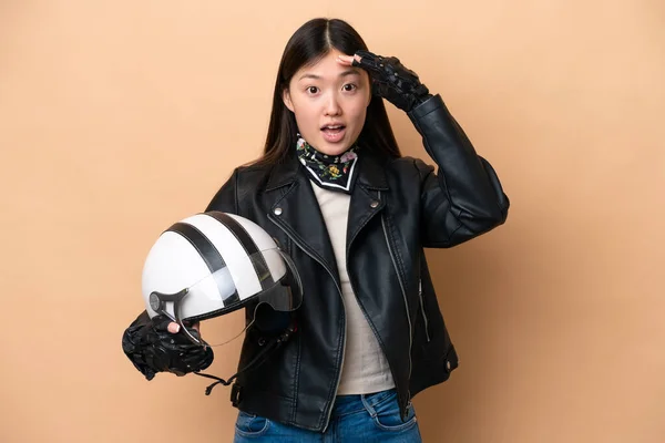 年轻的中国女人 戴着米色背景的摩托车头盔 一边看着侧面 一边做着令人惊讶的动作 — 图库照片