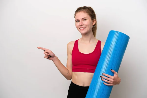 年轻的英国女运动员一边去上瑜伽课 一边拿着一块用白色背景隔开的垫子 手指指向旁边 — 图库照片