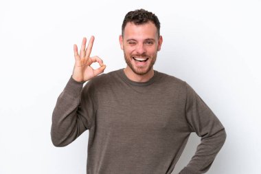 Beyaz arka planda izole edilmiş genç Brezilyalı adam parmaklarıyla tamam işareti gösteriyor