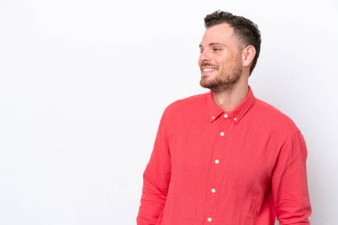 Genç Brezilyalı bir adam beyaz arka planda izole edilmiş, yana bakıyor ve gülümsüyor.