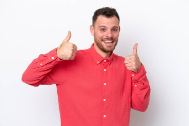 Beyaz arka planda izole edilmiş genç Brezilyalı bir adam baş parmak hareketi yapıyor.