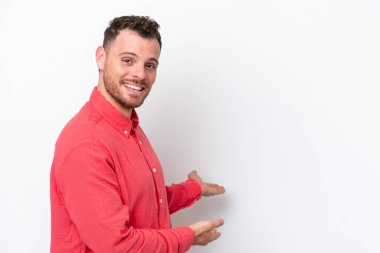 Beyaz arka planda izole edilmiş genç Brezilyalı adam, davet etmek için ellerini yana uzatıyor.