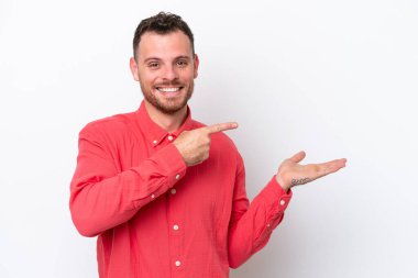 Beyaz arka planda izole edilmiş genç Brezilyalı bir adam bir ilan vermek için avucunun içinde hayali bir mekan tutuyor.