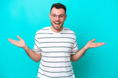 Genç Brezilyalı adam mavi arka planda izole edilmiş, şok olmuş yüz ifadesi var.