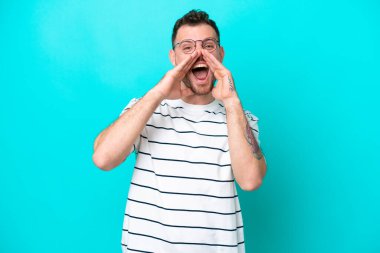 Genç Brezilyalı bir adam mavi arka planda izole edilmiş bağırıyor ve bir şey duyuruyor.