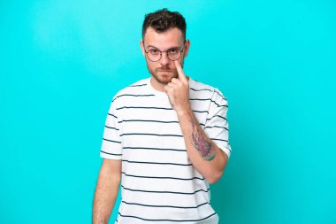 Mavi arka planda izole edilmiş genç Brezilyalı bir adam bir şey gösteriyor.