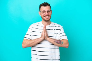 Mavi arka planda izole edilmiş genç Brezilyalı adam avuç içlerini bir arada tutuyor. İnsan bir şey ister.