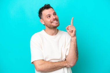 Mavi arka planda izole edilmiş genç Brezilyalı adam harika bir fikre işaret ediyor.