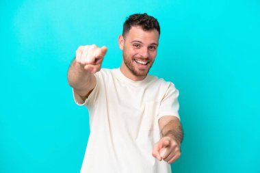 Mavi arka planda izole edilmiş genç Brezilyalı adam mutlu bir ifadeyle ön tarafı işaret ediyor.