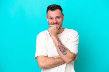 Mavi arka planda izole edilmiş genç Brezilyalı adam mutlu ve gülümsüyor.