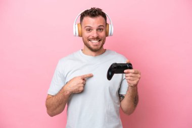 Pembe arka planda izole edilmiş bilgisayar oyunu kontrolörüyle oynayan Brezilyalı genç bir adam.