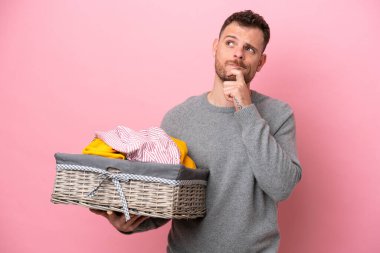 Genç Brezilyalı bir adam pembe arka planda soyutlanmış bir çamaşır sepetini tutuyor. Şüpheleri var ve düşünüyor.
