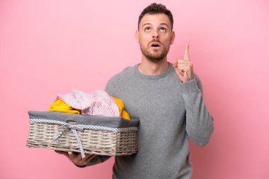 Genç Brezilyalı bir adam pembe arka planda izole edilmiş bir çamaşır sepeti tutuyor.