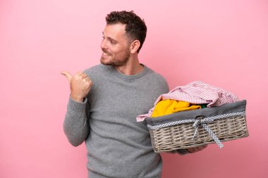 Genç Brezilyalı bir adam pembe arka planda izole edilmiş bir çamaşır sepeti tutuyor. Yan tarafı göstererek bir ürün sunuyor.