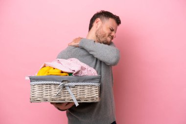 Genç Brezilyalı bir adam pembe arka planda izole edilmiş bir çamaşır sepetini tutuyor. Çabaladığı için omuz ağrısı çekiyor.