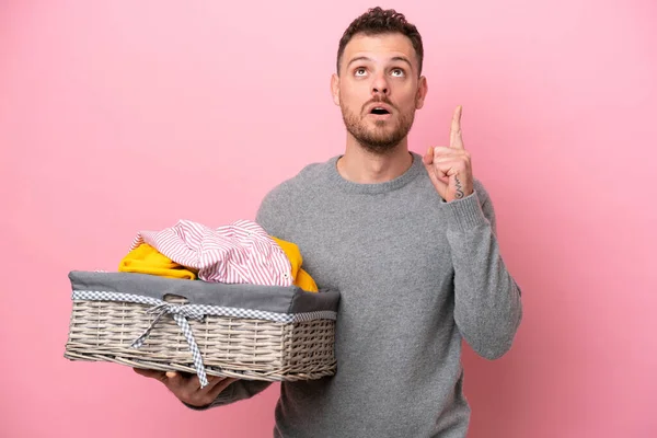 Genç Brezilyalı bir adam pembe arka planda izole edilmiş bir çamaşır sepeti tutuyor.