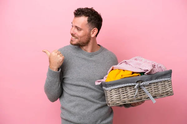 Genç Brezilyalı bir adam pembe arka planda izole edilmiş bir çamaşır sepeti tutuyor. Yan tarafı göstererek bir ürün sunuyor.