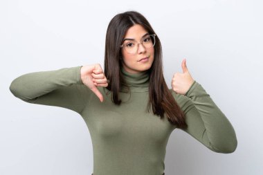 Beyaz arka planda izole edilmiş Brezilyalı genç bir kadın iyiye-kötüye işaret veriyor. Evet ya da hayır arasında kararsız