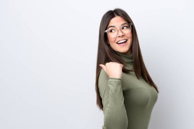 Beyaz arka planda izole edilmiş genç Brezilyalı kadın bir ürün sunmak için kenarı işaret ediyor