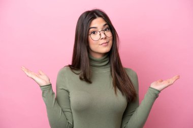 Genç Brezilyalı kadın pembe arka planda izole edilmiş gözlüklü ve şüpheleri var.