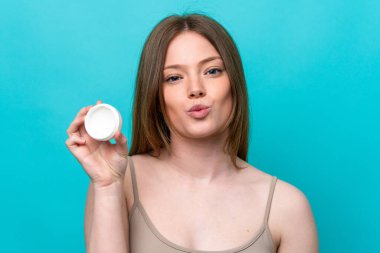 Genç beyaz kadın, mavi arka planda nemlendirici ile izole edilmiş.