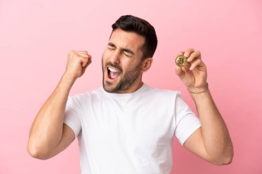 Pembe arka planda izole edilmiş Bitcoin tutan genç adam zaferi kutluyor.