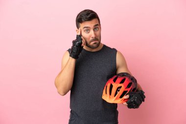 Pembe arka planda izole edilmiş genç bisikletçi bir fikir düşünüyor.