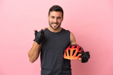 Pembe arka planda izole edilmiş genç bisikletçi baş parmak hareketi yapıyor.