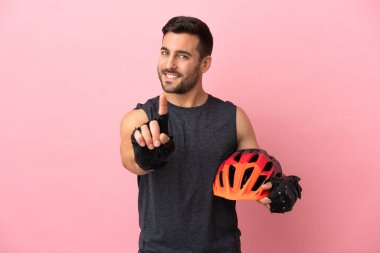 Pembe arka planda izole edilmiş genç bisikletçi parmağını kaldırıyor ve gösteriyor.