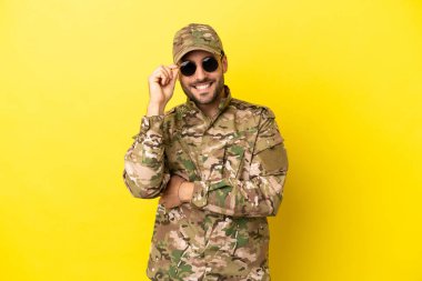 Sarı arka planda gözlüklü ve mutlu bir asker.